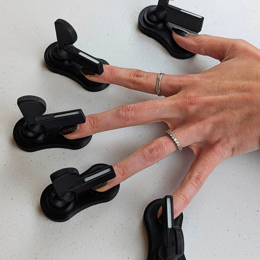 A hand with all five fingers positioned under adjustable magnetic arms for simultaneous hands-free nail polish magnetization on a white surface.