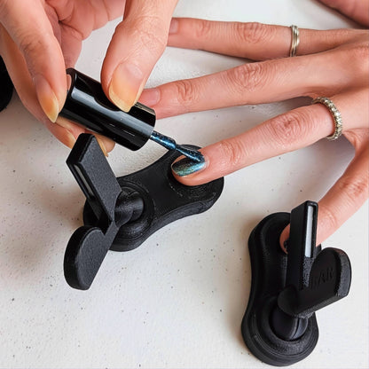 Close-up of a finger resting on a black magnetic tool base while blue magnetic nail polish is being applied for maximum stability.